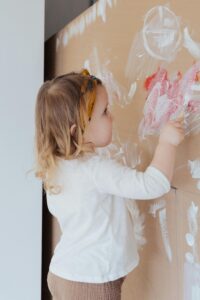 Young girl painting with creativity and enjoyment on a cardboard canvas indoors.