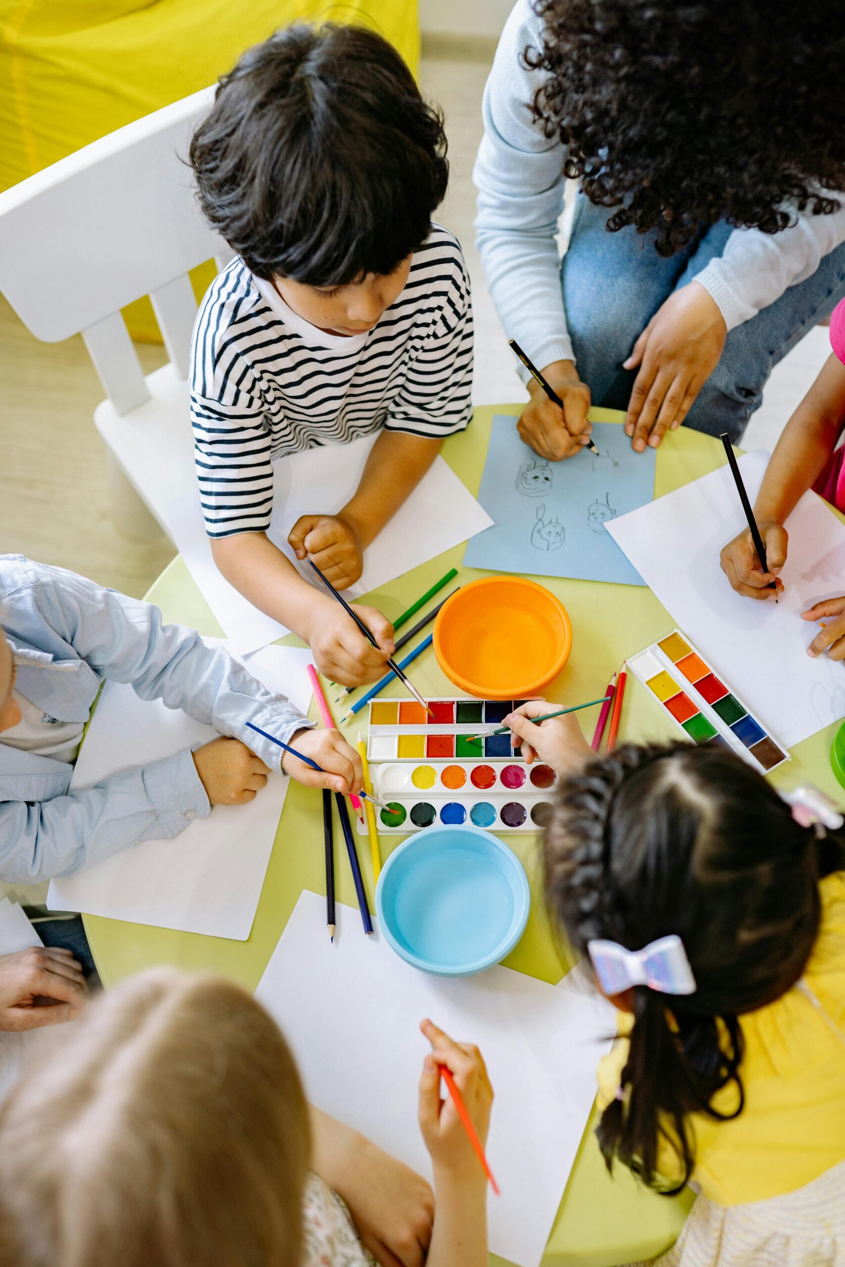 Top view of children painting with watercolors at a preschool art class.